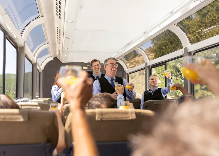 Passengers and staff toasting with orange juice in a luxury dome train car with panoramic windows.