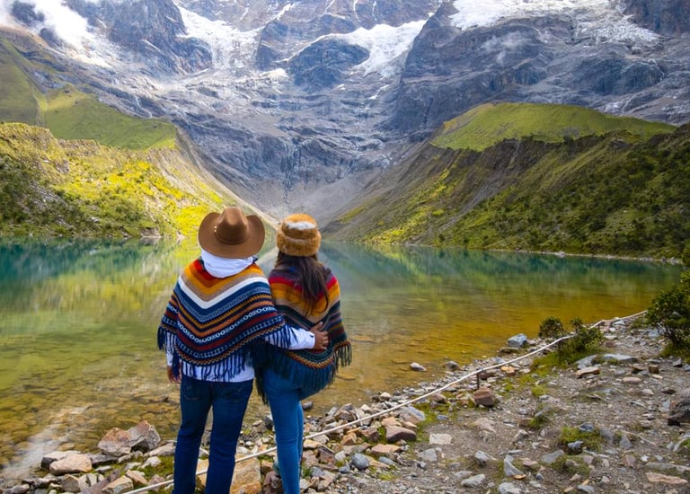 Couple in traditional ponchos overlooking Humantay Lake and snow-capped Andes mountains in Peru.