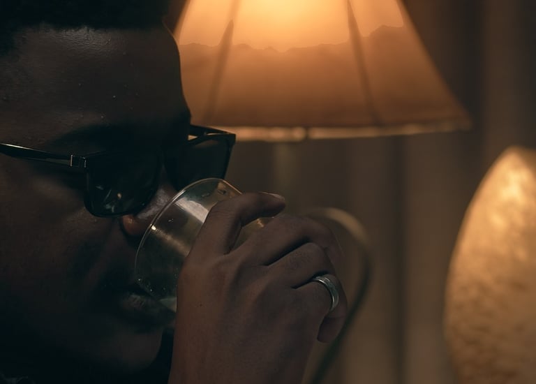 Cinematic frame from the short film Grief directed by Daniel da Trindade showing a man drinking in warm lamp light.
