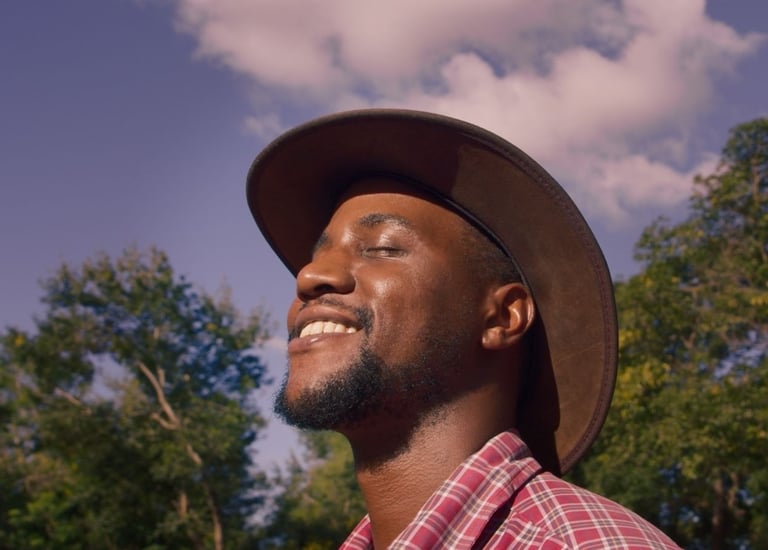 Portrait of a farmer smiling in warm sunlight, wearing a wide-brim hat outdoors.