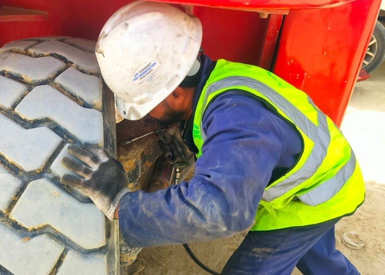 A construction worker in a hard hat and safety vest inspects a heavy machinery tire.