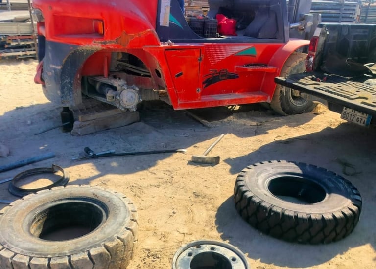 Red industrial forklift undergoing tire repair and maintenance at a sunny construction site.