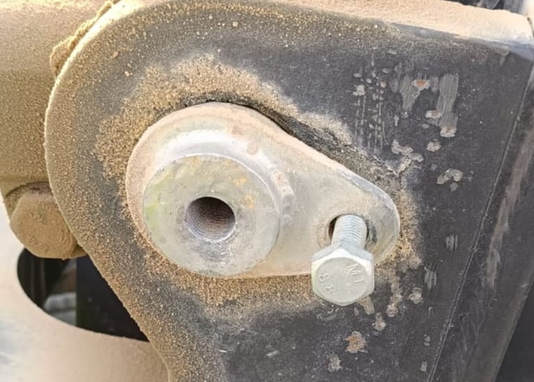 Close-up of a dusty metal pivot pin and hex bolt on heavy industrial machinery equipment.