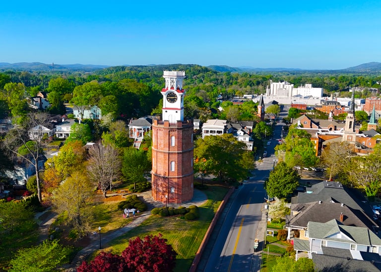 Aerial view of the historic brick Clock Tower in Rome, Georgia, surrounded by lush green trees and city streets.