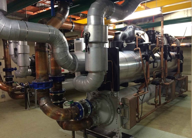 Industrial HVAC chiller system with insulated steel pipes and copper plumbing in a plant room.