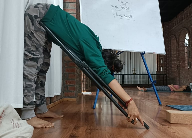 A person practicing yoga with a chair in a studio near a whiteboard for pranayama class.