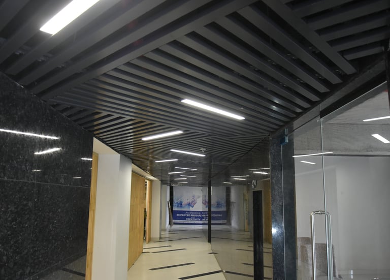 Modern office hallway with dark louvered ceiling, bright LED lights, and marble walls.