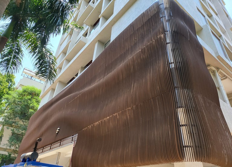 Modern building facade featuring a wavy brown metal architectural screen for sun shading and privacy.