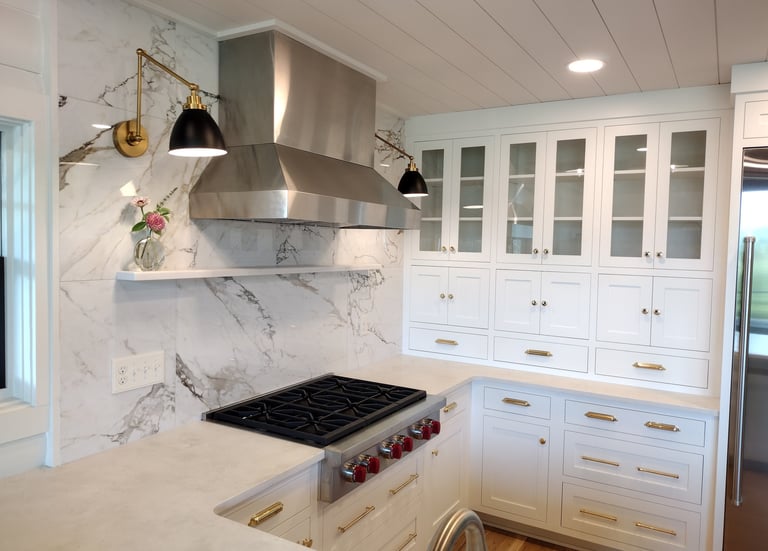 Modern white kitchen featuring a marble backsplash, stainless steel range hood, and gold hardware accents.