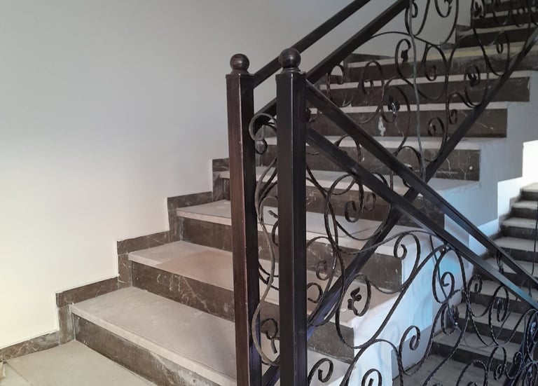 Elegant marble staircase featuring custom wrought iron railings with decorative scrollwork.
