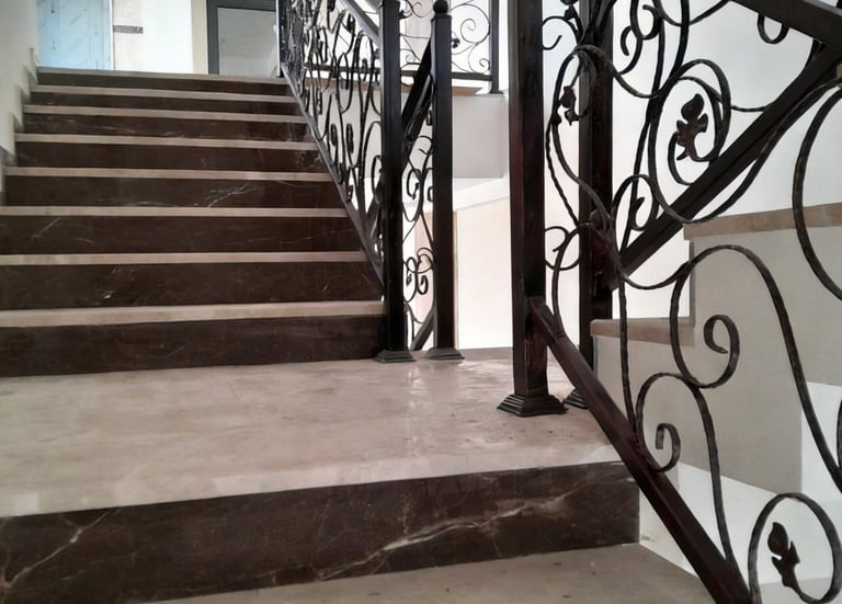 Elegant marble staircase with ornate black wrought iron handrails in a modern interior.