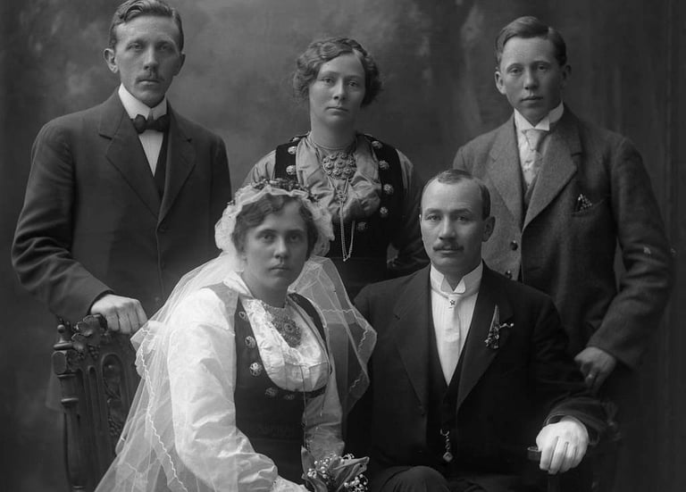 Two mend and a woman stand behind a bride and groom, black and white, the women in bunad