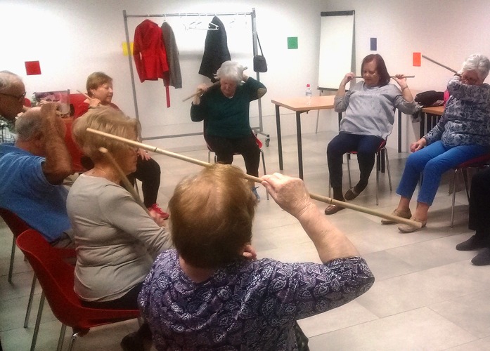 Un grupo de personas mayores está sentado en círculo realizando ejercicios de movimiento para mejora
