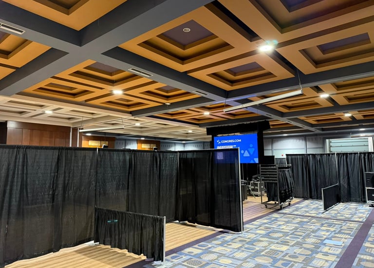 Professional conference room setup with black pipe and drape partitions, carpeted floors, and a coffered ceiling.