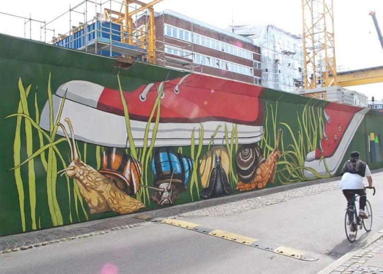 Urban street art mural featuring a giant red sneaker stepping over colorful snails on a green wall.