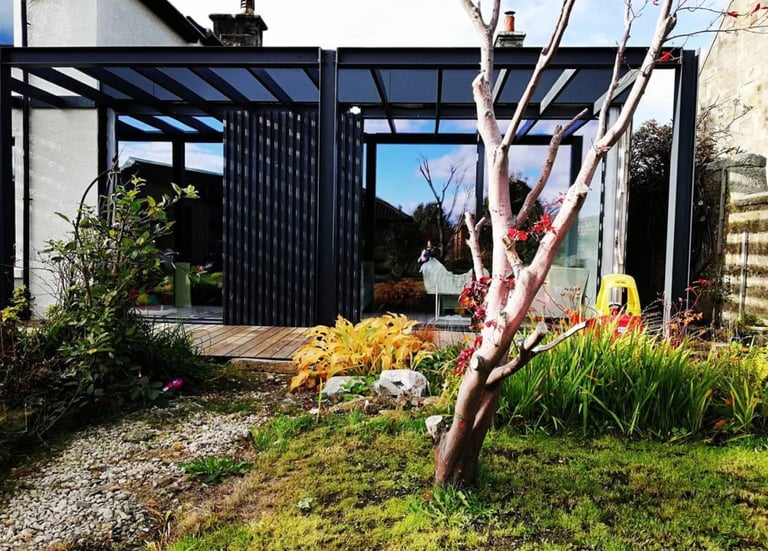 Modern black timber slat garden room extension with sliding doors and wooden decking.