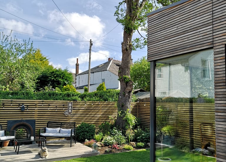 Modern garden design featuring a timber-clad garden room, wooden slatted fence, and a sunny lawn area.