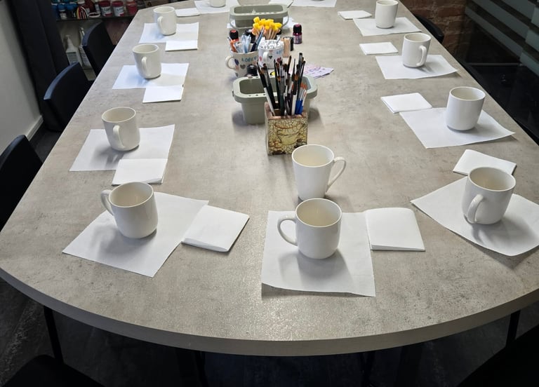 White ceramic mugs and paintbrushes on a table for a pottery painting workshop.