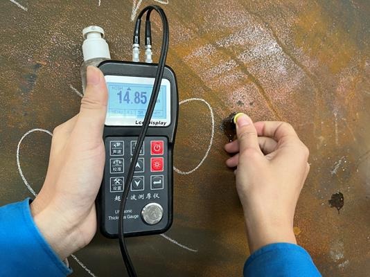 Technician performing ultrasonic thickness testing on an ISO tank using a digital gauge