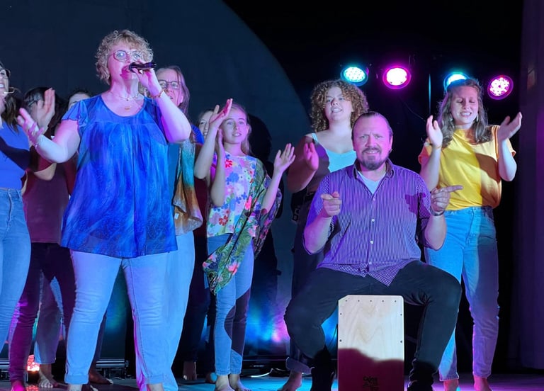 eine Gruppe auf der Bühne, singend, klatschend, ein Mann mit der Cajon dabei