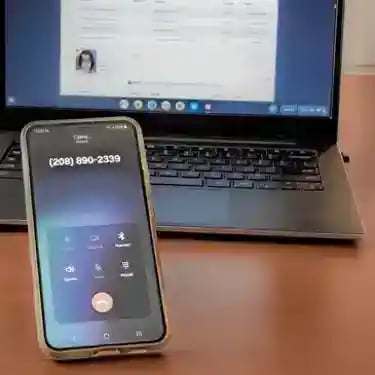 A smartphone displaying an active phone call to bail bondsman next to an open laptop.