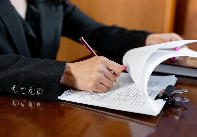 Abogado profesional con traje negro firma documentos legales con un bolígrafo en un escritorio