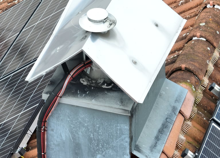 Close-up of a stainless steel chimney cap and solar panel installation on a tiled roof.