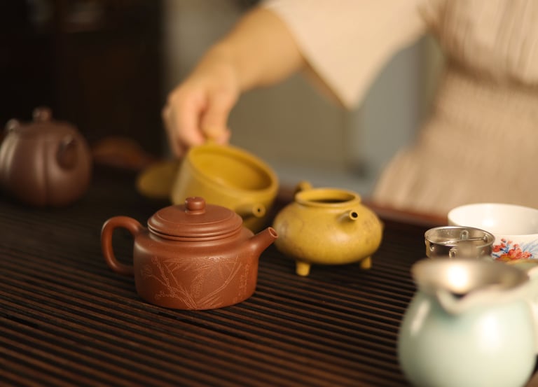 Person pouring water from a teapot with cups and a tea strainer on a wooden table
