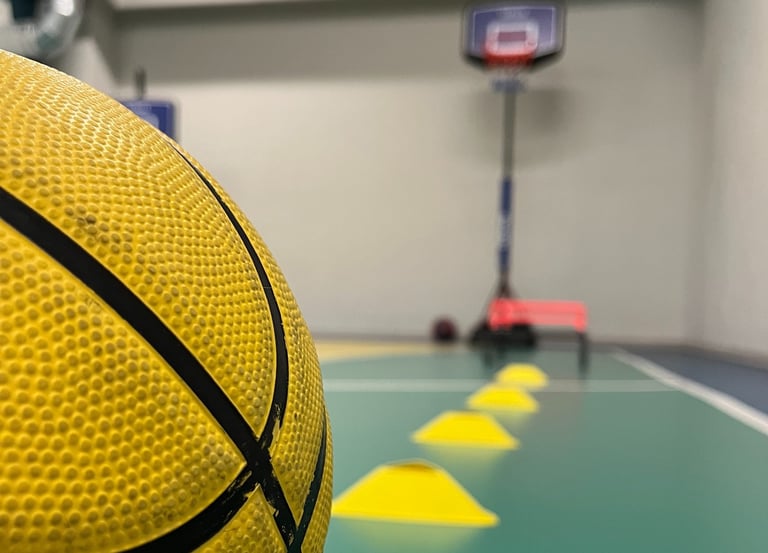 Primo piano di un pallone da basket giallo in un'area multisport della palestra Move 2 Grow a Milano, con coni e canestro sul