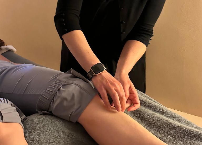 Acupuncturist inserting needle into patient’s lower leg on acupuncture table. 