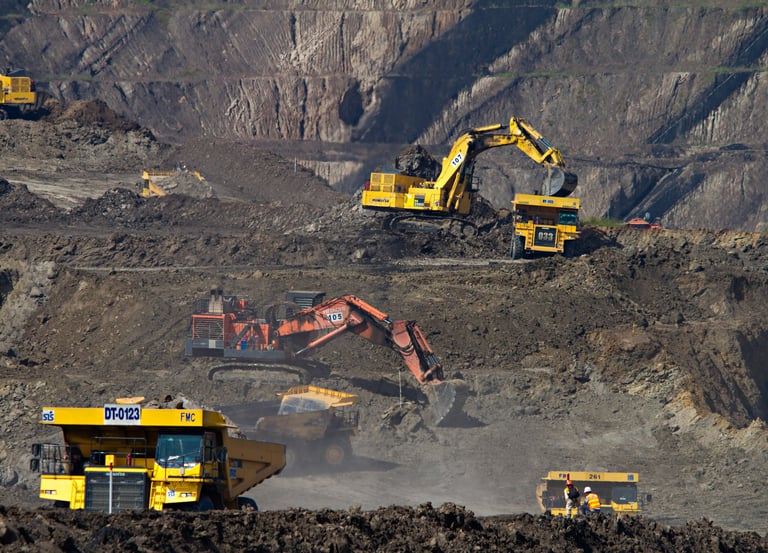 Heavy hydraulic excavators loading earth into large yellow haul trucks at a busy open-pit mining site.