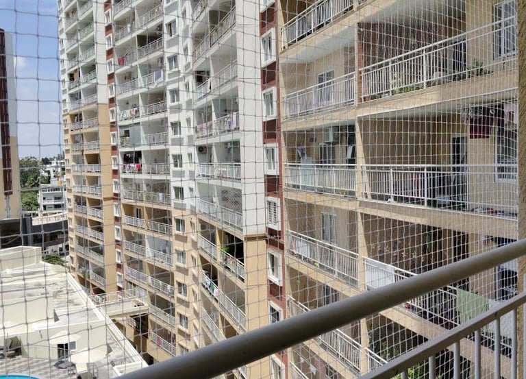 A technician carefully installing a sturdy safety net on a high-rise balcony in Hebbal.