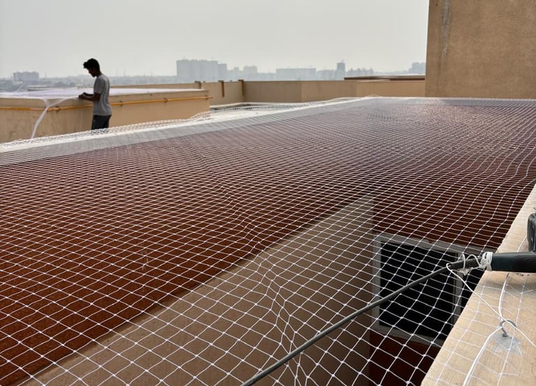A technician carefully installing a sturdy safety net on a balcony in a Bengaluru apartment.