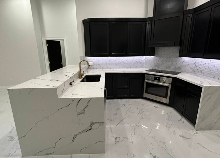 Modern luxury kitchen featuring black cabinets, white marble waterfall island, and matching marble flooring.