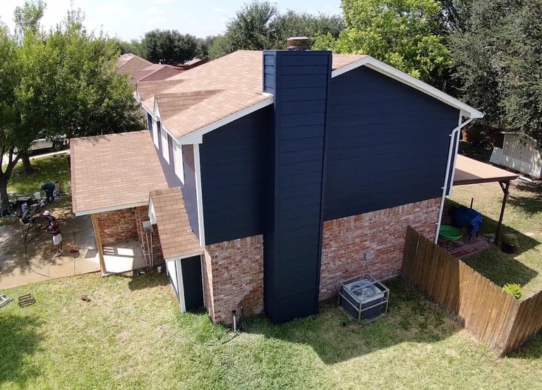 Aerial view of a suburban home featuring navy blue siding, brick exterior, and a new brown shingle roof.