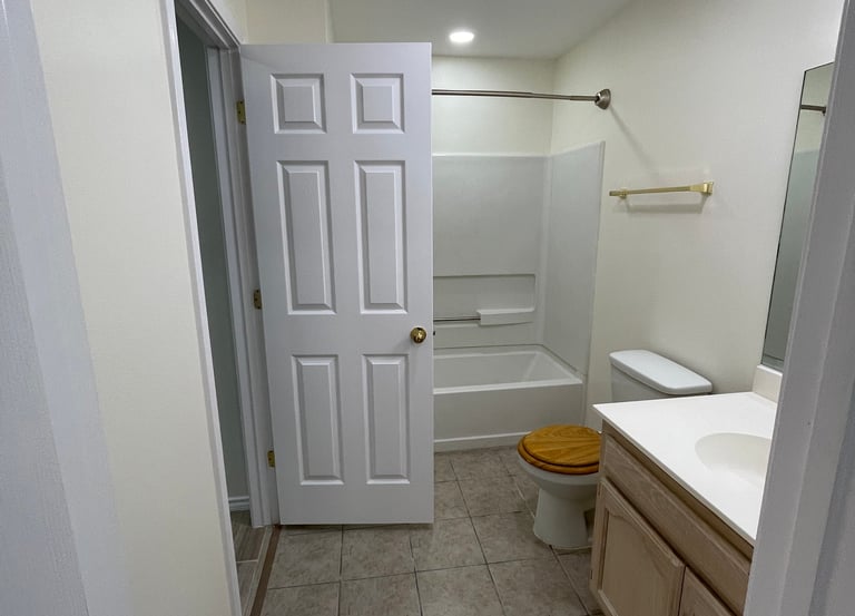 A modern bathroom remodel featuring a neutral tile floor, white bathtub, and light wood vanity.