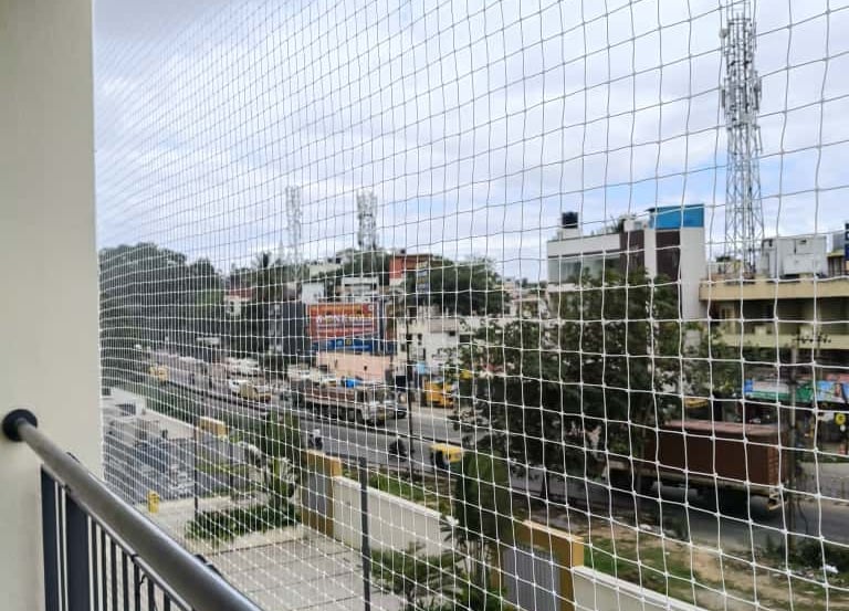 A close-up of a sturdy pigeon net installed on a balcony overlooking a busy street in Chennai.