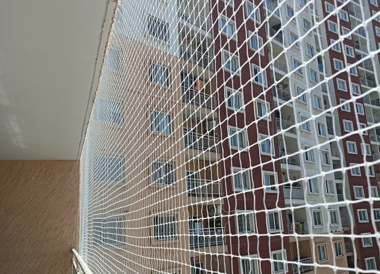 A skilled technician from Arjilli Enterprises installing a sturdy pigeon net on a balcony overlookin