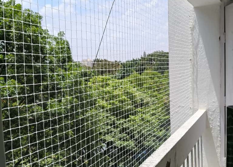 A technician carefully installing a strong safety net on a building balcony in Chennai.