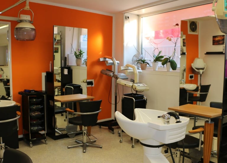Professional hair salon interior with orange walls, styling chairs, and white shampoo basins.