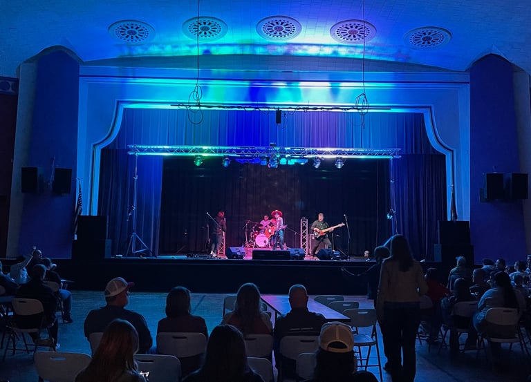 Live band performing on stage at an Memorial Hall with blue and green stage lighting and audience.