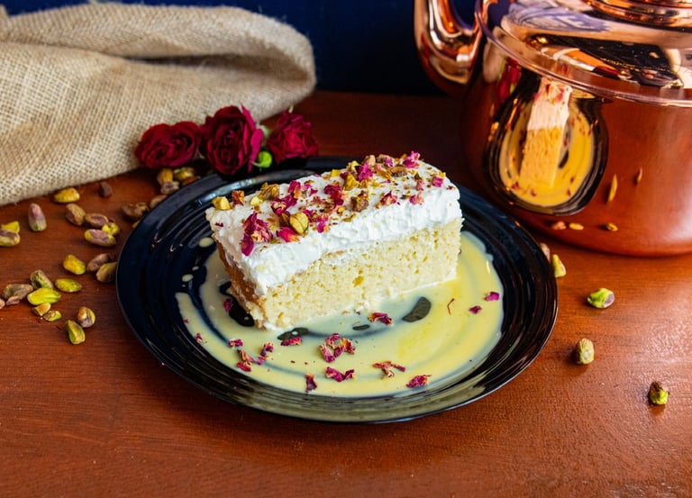 Indian Fusion Dessert Kulfi Tres Leches on a plate with a chai bronze kettle and roses and pistachio