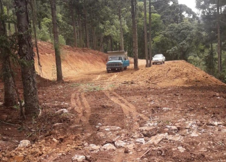 a truck driving down a dirt road with a truck in the background