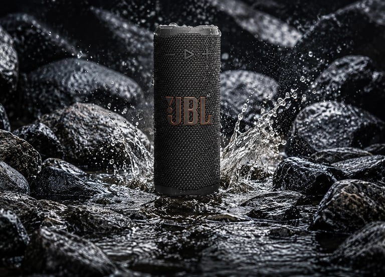 Enceinte JBL étanche noire avec gouttes d’eau, photo produit HDR ultra détaillée sur rochers mouillés.