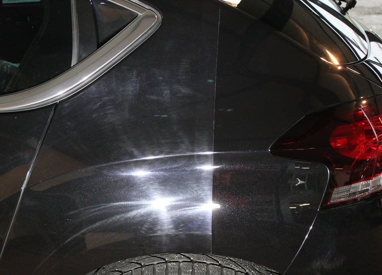 Carrosserie d'une voiture noire polie et lustrée, reflétant la lumière pour une finition miroir impe