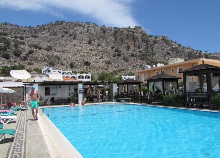 Luxury swimming pool at a Mediterranean resort with mountains and cabanas in the background.