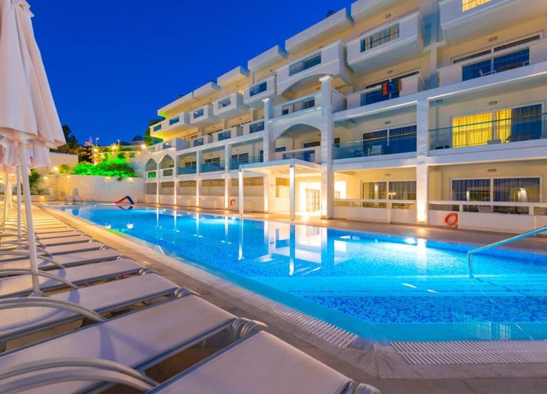 Luxury resort swimming pool illuminated at night with rows of sun loungers and hotel balconies.