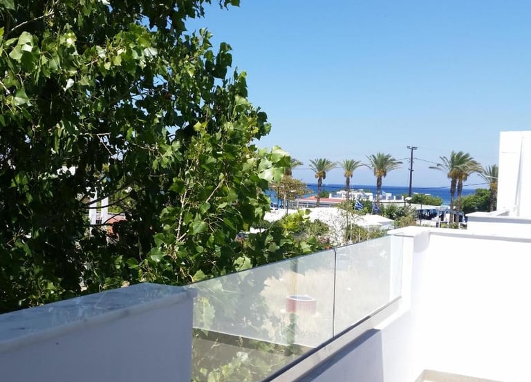 Modern white hotel balcony with glass railing overlooking palm trees and the blue ocean.