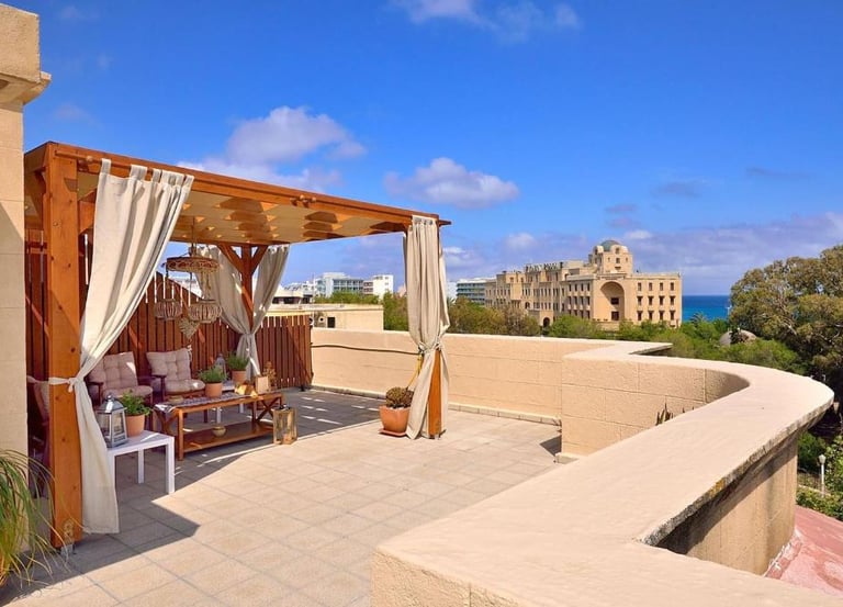 Luxury rooftop terrace with wooden pergola and sea view overlooking a Mediterranean coastal city.