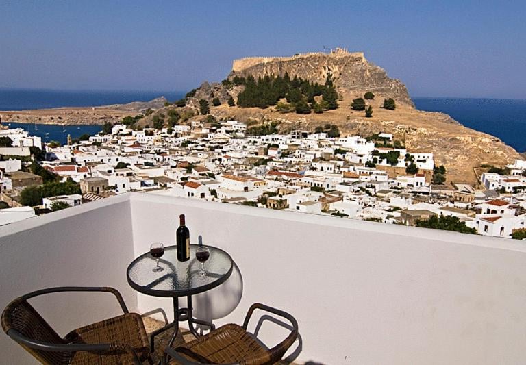 Wine on a balcony overlooking the Lindos Acropolis and whitewashed village in Rhodes, Greece.